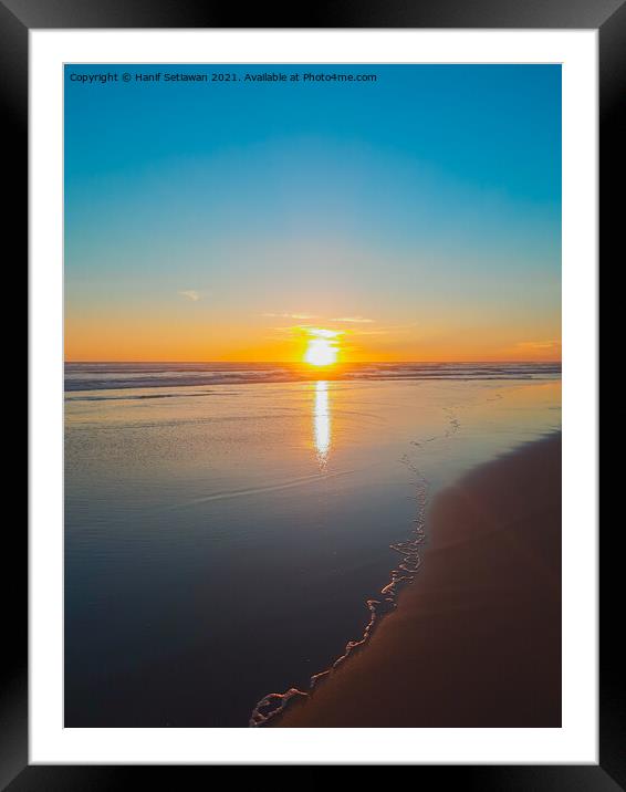 Wide sand beach reflecting orange sunset sunlight. Framed Mounted Print by Hanif Setiawan