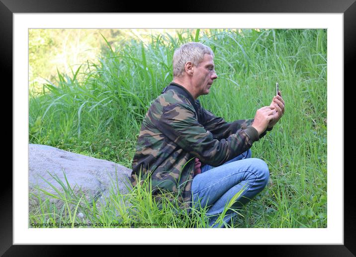 A Caucasian senior man using his phone in a meadow Framed Mounted Print by Hanif Setiawan