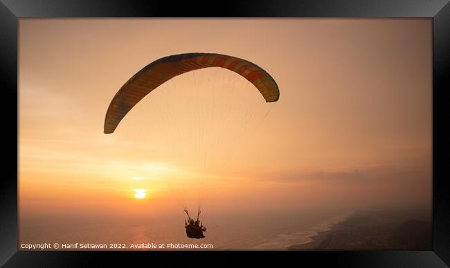 Tandem paragliding over sea and beach while golden Framed Print by Hanif Setiawan