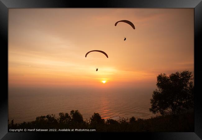 Two paraglider over treetops and ocean at sunset Framed Print by Hanif Setiawan