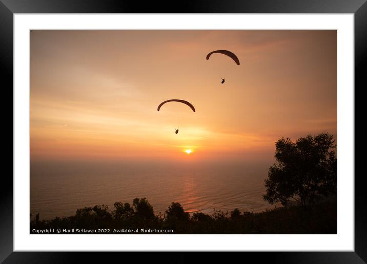 Two paraglider over treetops and ocean at sunset Framed Mounted Print by Hanif Setiawan