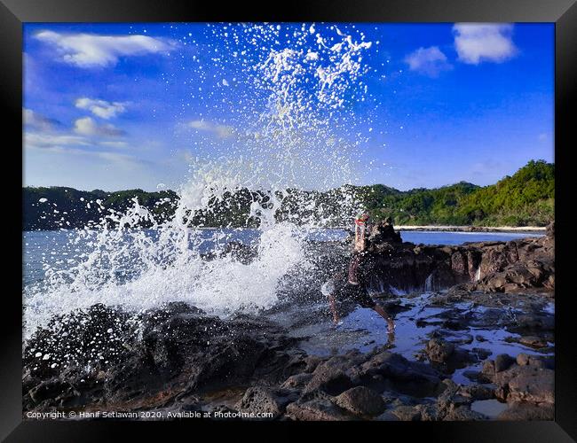 A big wave hits a man on a rock plateau Framed Print by Hanif Setiawan