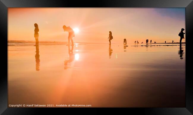 Silhouetted people in a row on a wet sand beach. Framed Print by Hanif Setiawan