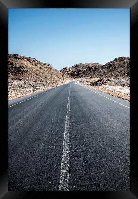 An empty tarmac road going thru arid mountains in  Framed Print by David GABIS