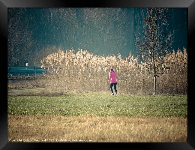 Woman in a pink jacket jogging in the park with dried reed grass background Framed Print by Ingo Menhard