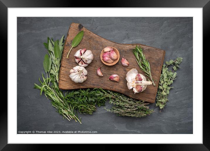 Still life, Garlic on a chopping board with herbs Framed Mounted Print by Thomas Klee