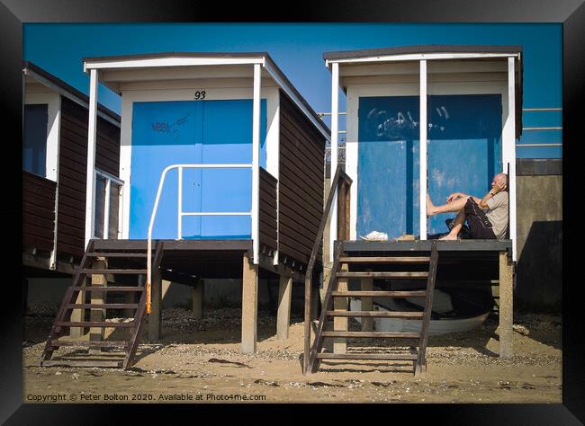 Beach huts at Thorpe Bay, Essex, with a person sitting on the floor talking on the phone. Framed Print by Peter Bolton