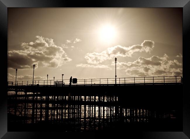 Sepia image of part of Southend Pier shot against the sun, with silhouette of structure and a man on the walkway. Southrnd on Sea, Essex. Framed Print by Peter Bolton
