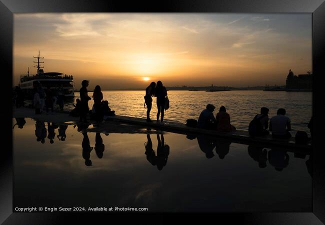 Silhouettes of some young people with beautiful reflections on the water at sunset Framed Print by Engin Sezer