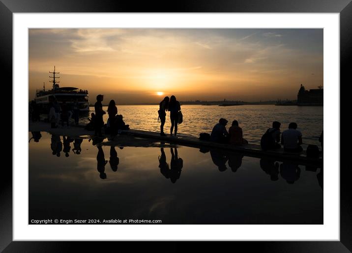 Silhouettes of some young people with beautiful reflections on the water at sunset Framed Mounted Print by Engin Sezer