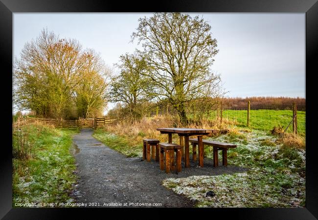Wooden table and chairs at a seating area on a countryside trail in winter Framed Print by SnapT Photography