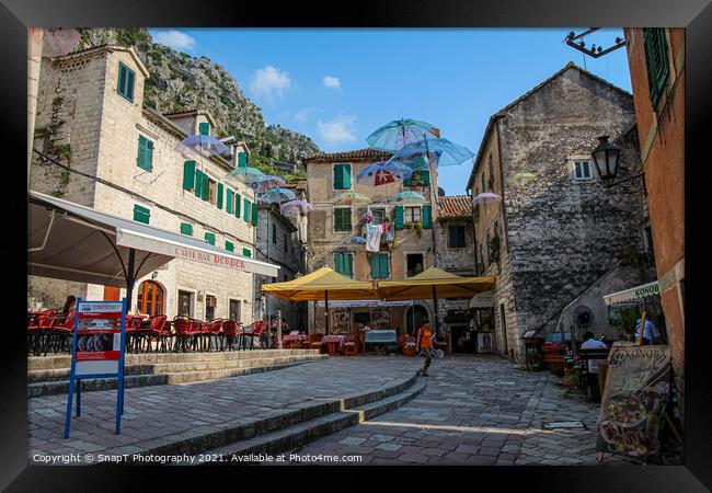 Cafe's and flying umbrellas on a square in the old town of Kotor, Montenegro Framed Print by SnapT Photography