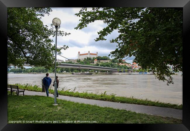 People walking along a footpath by the River Danube with the Bratislava Castle Framed Print by SnapT Photography