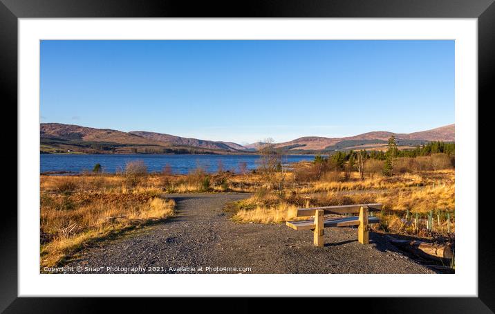 A wooden bench overlooking Clatteringshaws Loch on a sunny winters day Framed Mounted Print by SnapT Photography