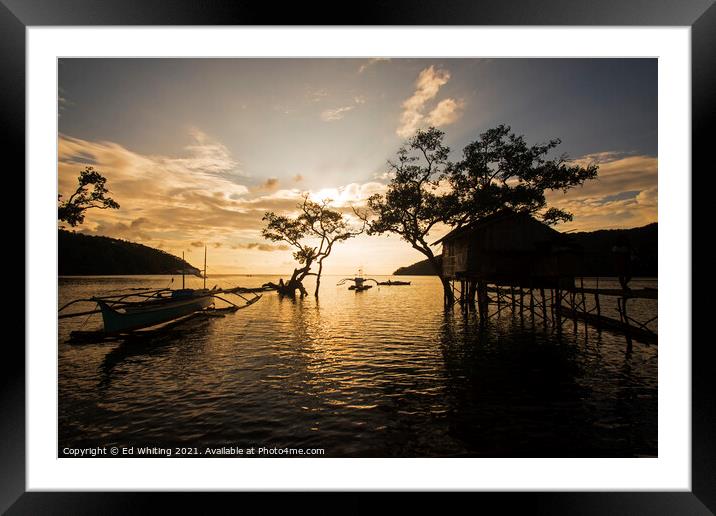A boat is docked next to the fisherman's home in sunset. Framed Mounted Print by Ed Whiting
