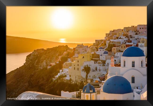 Blue domed churches and traditional white houses facing Aegean Sea with warm sunset light in Oia, Santorini, Greece Framed Print by Chun Ju Wu