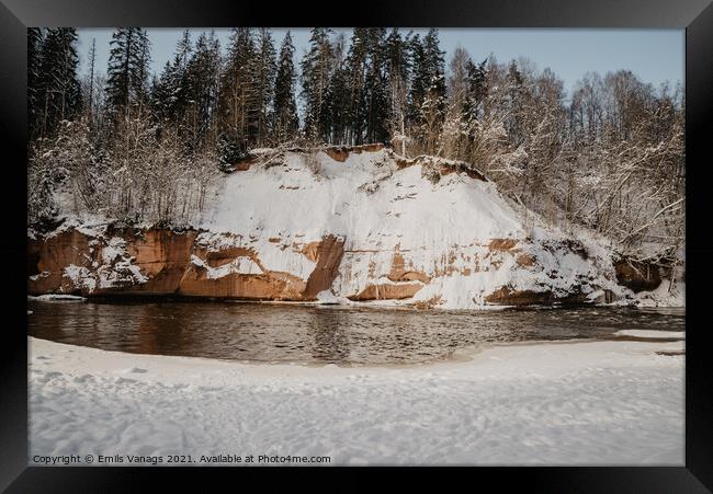 rock cliff and cave by the river Gauja in the Gauja National Park in Latvia in winter with beautiful sun through the forest Framed Print by Emils Vanags