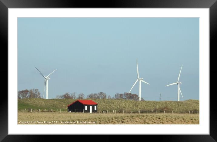 Black hut with red roof and wind turbines at Rye Harbour Framed Mounted Print by Joan Rosie