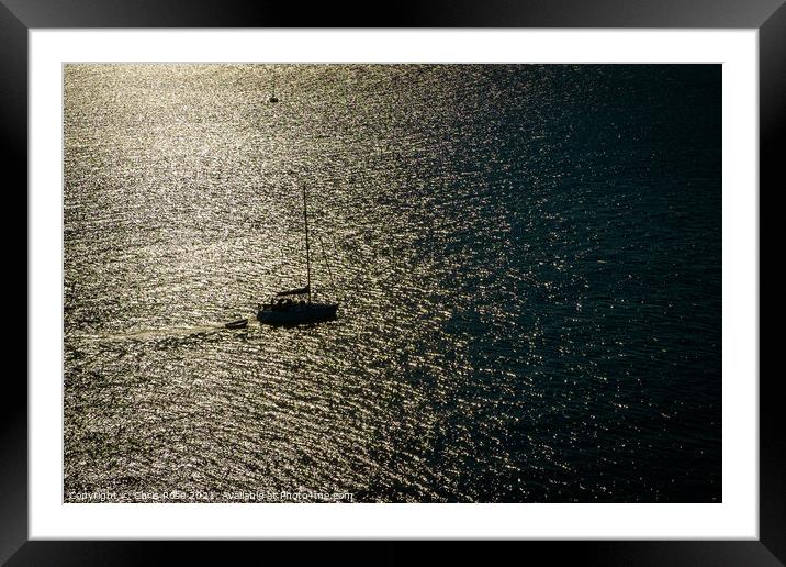 A silhouetted sailing boat motors out Framed Mounted Print by Chris Rose