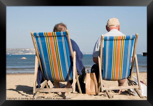 Elderly couple in bright striped deckchairs on the sand at Weymouth Framed Print by Gordon Dixon