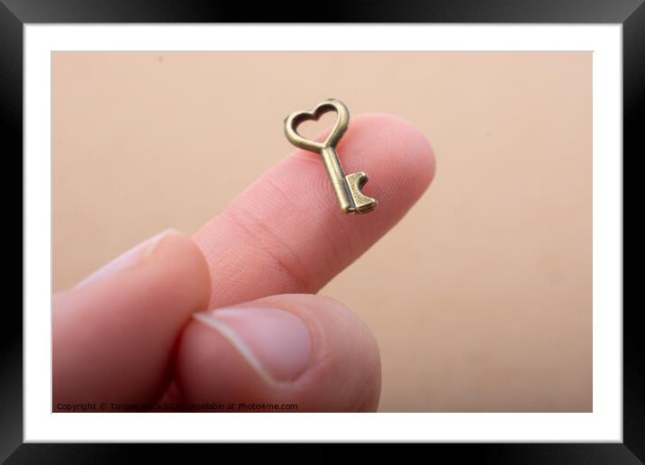 Tiny key with heart shape on the finger tip Framed Mounted Print by Turgay Koca