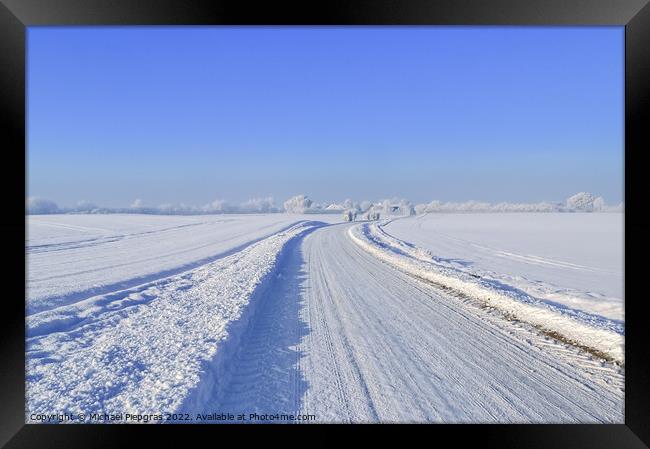 View of a snow-covered country road in winter with sunshine and blue sky Framed Print by Michael Piepgras