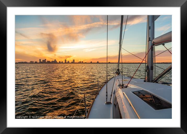 Yacht sailing towards cityscape on horizon at sunset Framed Mounted Print by Spotmatik 