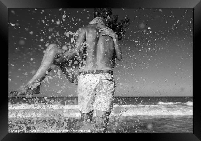 Fun loving ethnic couple running in ocean waves Framed Print by Spotmatik 