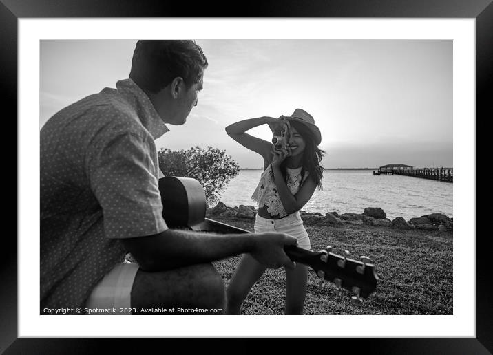 Smiling female taking photograph of partner playing guitar Framed Mounted Print by Spotmatik 