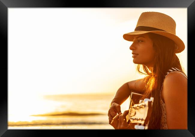 Indian woman wearing hat playing guitar on beach Framed Print by Spotmatik 
