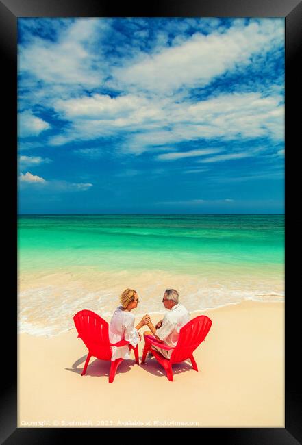 Mature couple on red chairs by ocean Bahamas Framed Print by Spotmatik 
