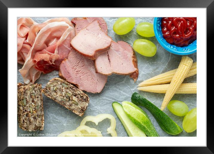 Cold appetizer. Cold cuts. Different snacks on a white crumpled paper, bacon, fruits, grapes, vegetables, from above. Framed Mounted Print by Lubos Chlubny
