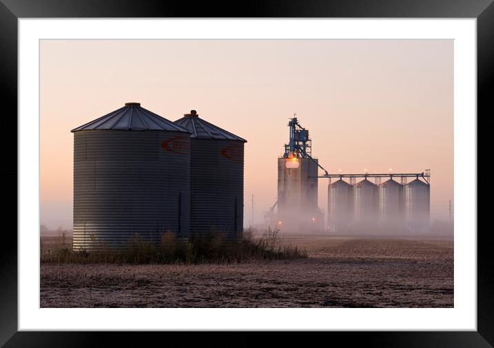 grain storage bins in a harvested soybean field with inland grain terminal in the background Framed Mounted Print by Dave Reede