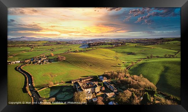 Aerial view of a picturesque rural landscape at sunset with vibrant green fields, a small village, and a winding road. Framed Print by Man And Life