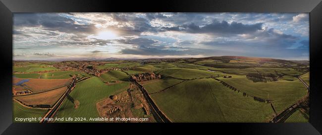 Panoramic aerial view of a scenic landscape with rolling hills, fields, and a winding road under a dramatic sky at sunset. Framed Print by Man And Life
