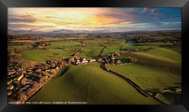 Aerial view of a scenic countryside at sunset with lush green fields, a small village, and a winding road leading towards distant hills. Framed Print by Man And Life