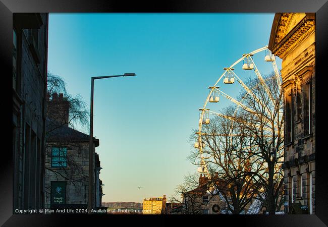 Urban sunset scene with silhouette of a Ferris wheel against a clear sky, flanked by historic buildings and a street lamp in Lancaster. Framed Print by Man And Life