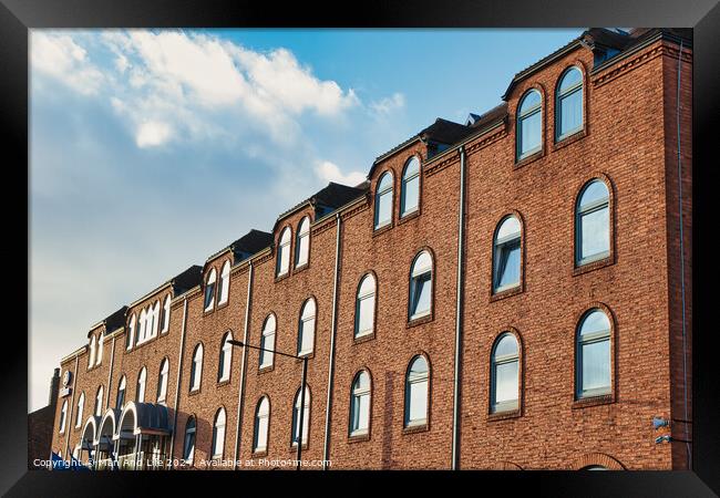 Row of traditional brick buildings against a blue sky with clouds in York, UK. Framed Print by Man And Life