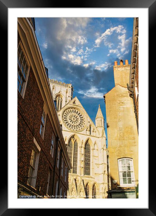 Historic cathedral facade with rose window, framed by old buildings against a blue sky with clouds in York, UK. Framed Mounted Print by Man And Life