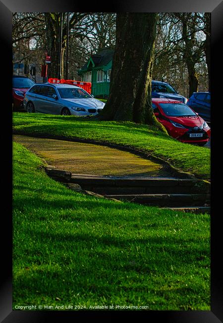 Sunny park with green grass and a pathway leading through trees, with parked cars in the background in Harrogate, England. Framed Print by Man And Life