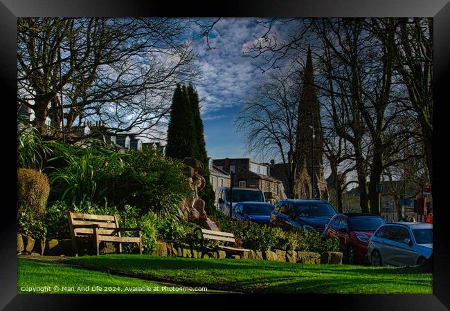 Tranquil urban park scene with benches and lush greenery, set against a backdrop of historic buildings and blue sky with wispy clouds in Harrogate, England. Framed Print by Man And Life