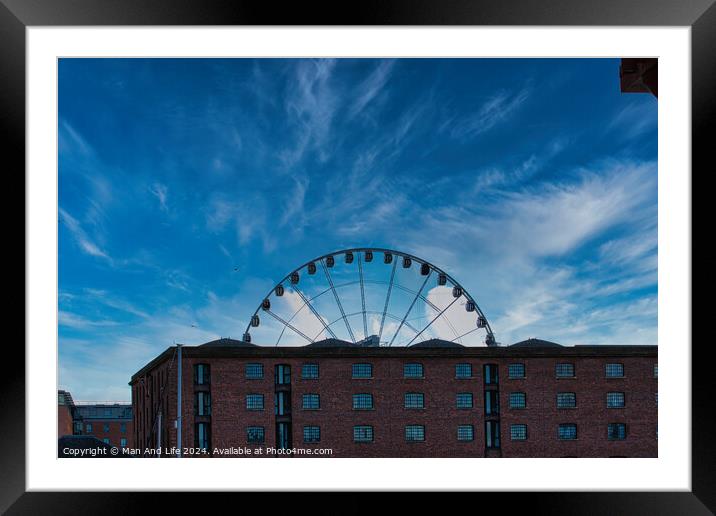 Ferris wheel silhouette against a blue sky with wispy clouds, framed by buildings in Liverpool, UK. Framed Mounted Print by Man And Life