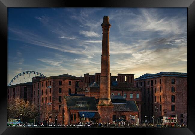 Historic red brick buildings with tall chimney against a dramatic sunset sky, with a Ferris wheel in the background in Liverpool, UK. Framed Print by Man And Life
