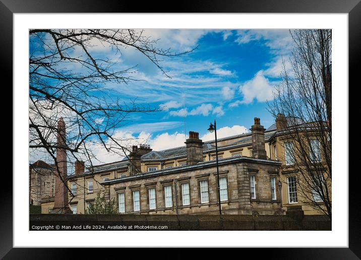 Classic European architecture with ornate details under a vibrant blue sky with fluffy clouds, framed by bare tree branches on the left in York, North Yorkshire, England. Framed Mounted Print by Man And Life