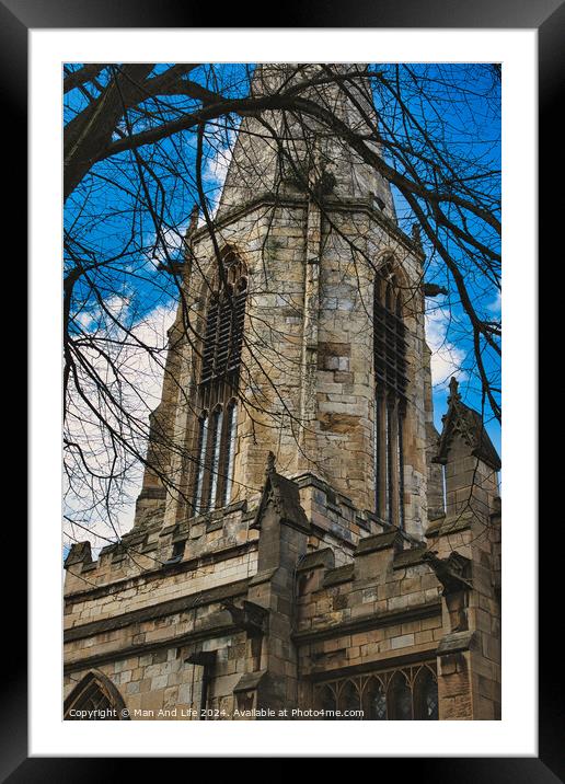 Gothic church tower with intricate stone details, framed by bare tree branches against a blue sky with fluffy clouds in York, North Yorkshire, England. Framed Mounted Print by Man And Life