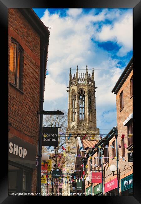 Quaint urban street with festive bunting leading to a historic church tower under a blue sky with fluffy clouds in York, North Yorkshire, England. Framed Print by Man And Life