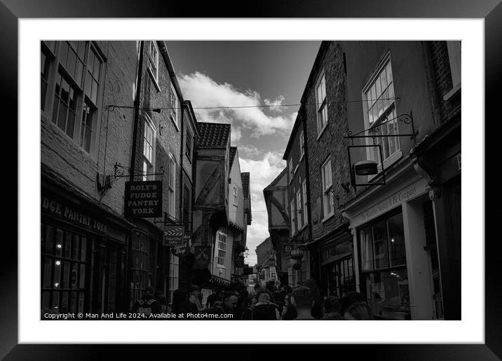 Black and white image of a bustling narrow street in York, with historic buildings, quaint shops, and pedestrians exploring the charming old town in York, North Yorkshire, England. Framed Mounted Print by Man And Life