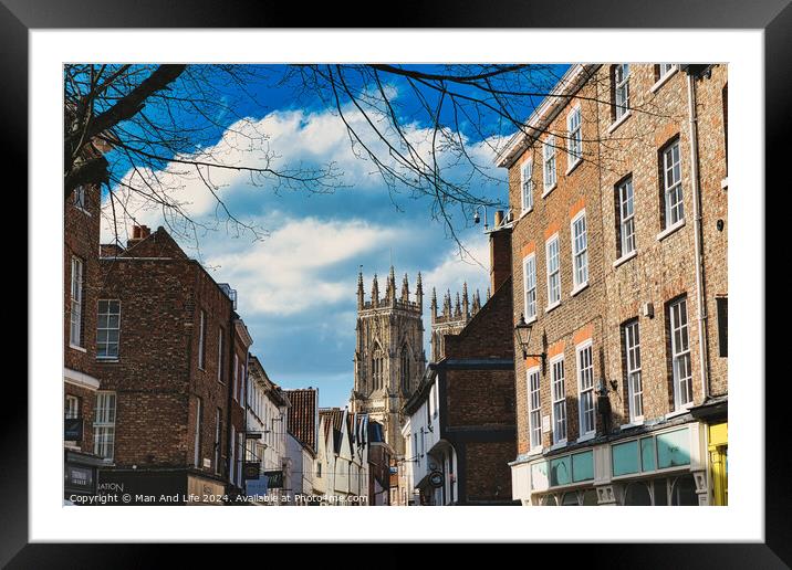 Historic European city street with traditional brick buildings and a prominent Gothic cathedral in the background under a blue sky with clouds in York, North Yorkshire, England. Framed Mounted Print by Man And Life