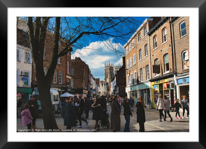 Bustling city street scene with pedestrians, historic buildings, and a cathedral spire under a blue sky with scattered clouds in York, North Yorkshire, England. Framed Mounted Print by Man And Life