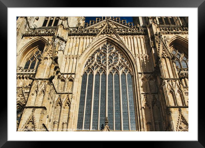 Gothic architecture detail of a cathedral's facade, featuring a large stained glass window and ornate stone carvings under clear skies in York, North Yorkshire, England. Framed Mounted Print by Man And Life